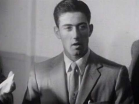 Tennis champion Ken Rosewall, dressed in a suit and tie, addresses the media.