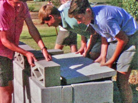 A group of young men and boys are building a backyard BBQ using cement besser blocks