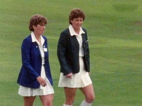 The two captains from the English and Australian women's cricket teams in 1987, Carol Hodges (England) and Lyn Larsen (Australia) walking across a cricket field. They are dressed in white cricket uniforms with their team blazers over the top.