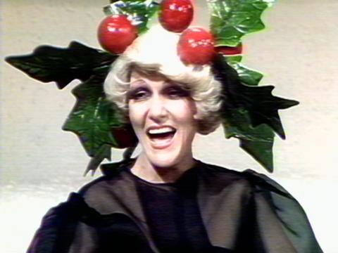 Jeanne Little wears a huge holly garland on her head. She is laughing.