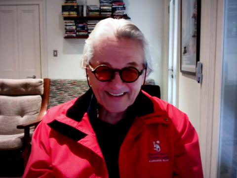 Head and shoulders shot of older man wearing glasses and red jacket looking directly at camera smiling