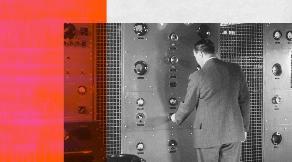 A man, pictured from behind, standing at a large console in a radio studio.