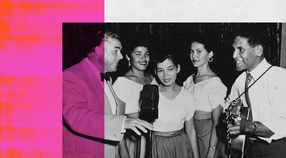 Amateur Hour host Terry Dear standing next to a band of 3 women and 1 man, they are standing around a microphone.