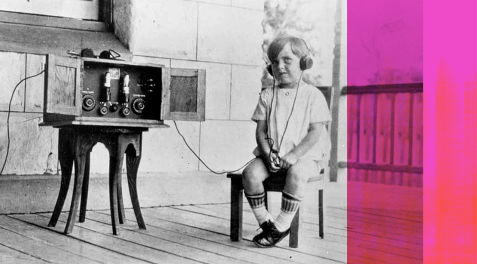 A young boy sitting on a chair wearing headphones and listening to an old radio