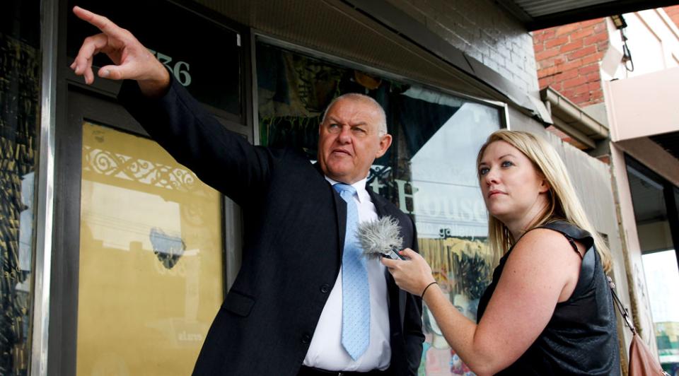 Rachael Brown interviewing policeman Ron Iddles in front of a store on a street.