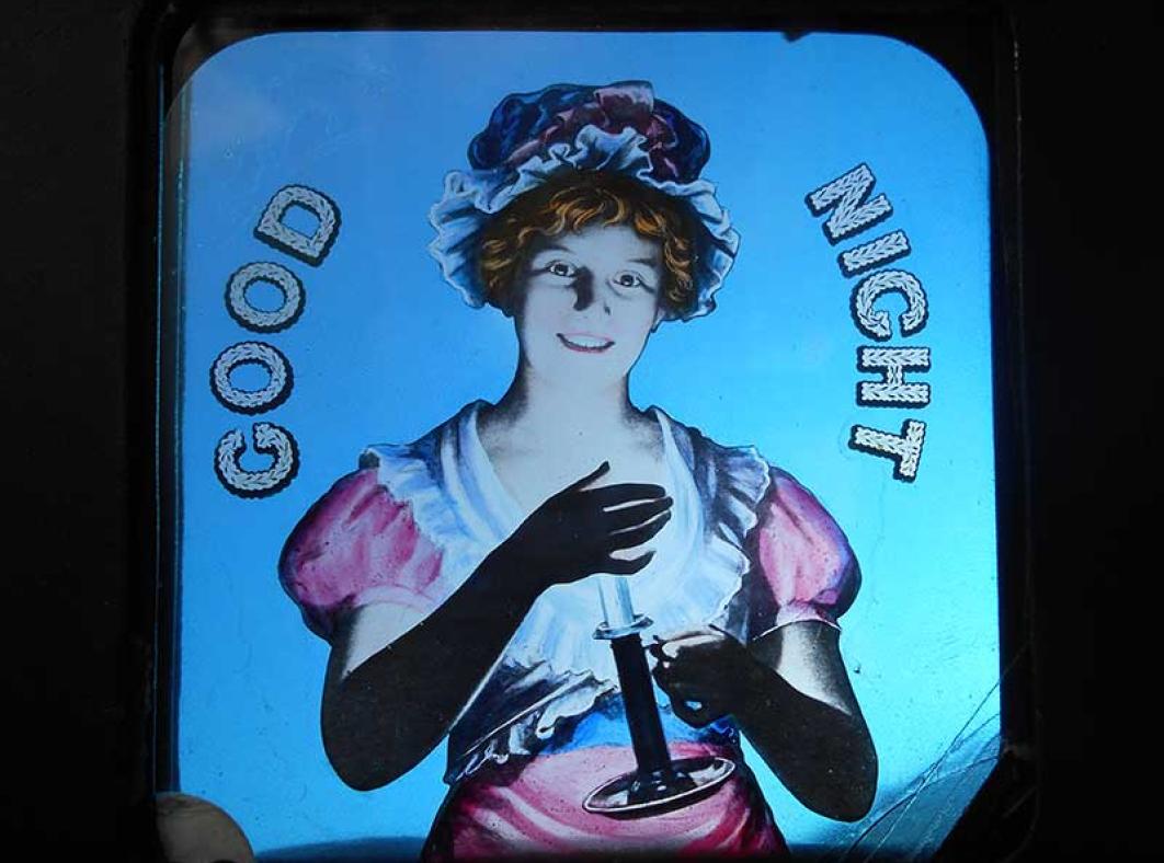 A glass slide with an image of a young woman holding a candle and smiling. The words 'GOOD NIGHT' are written on the slide.