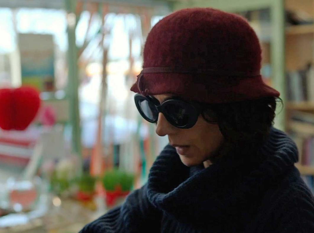 A woman in a hat and dark glasses looking down towards the floor in a grocery store.