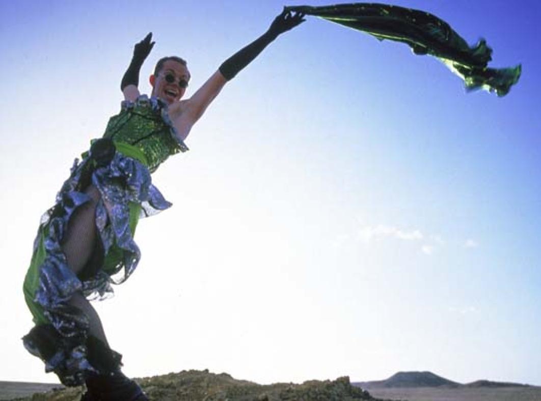 Hugo Weaving in a green dress leaning back on a desert rock and waving a scarf in the air above his head in a scene from the film The Adventures of Priscilla, Queen of the Desert