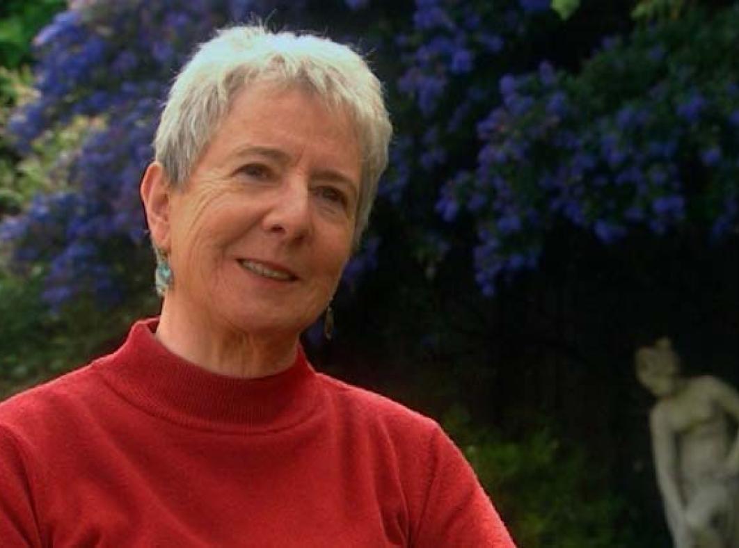 A woman wearing a red jumper being interviewed while seated in a garden outdoors