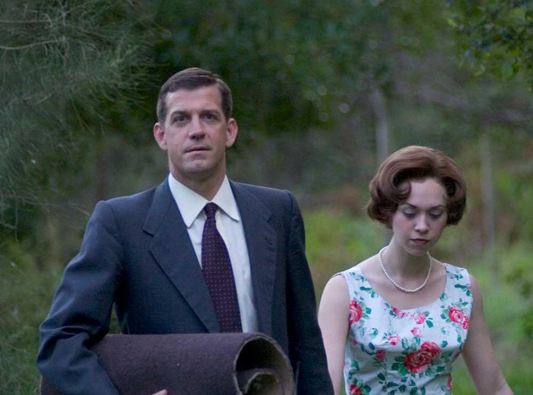 A well-dressed woman and man walking through a bush area.