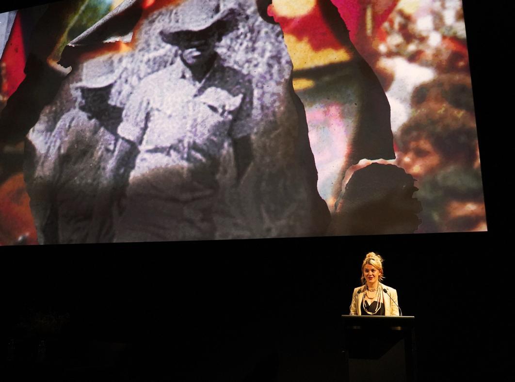 Jazz Money standing at a lectern in front of a cinema screen displaying an image from their film WINHANGANHA
