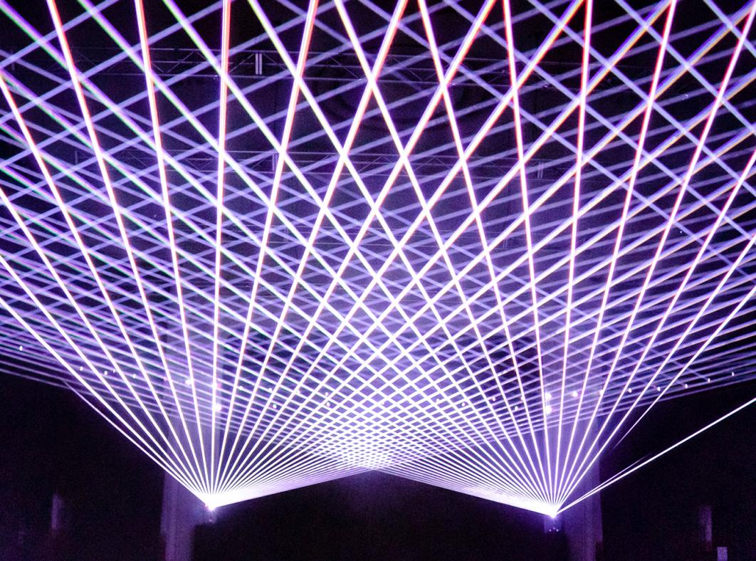 An array of criss-crossing purple-white laser beams directed towards the ceiling in the Constellations exhibition