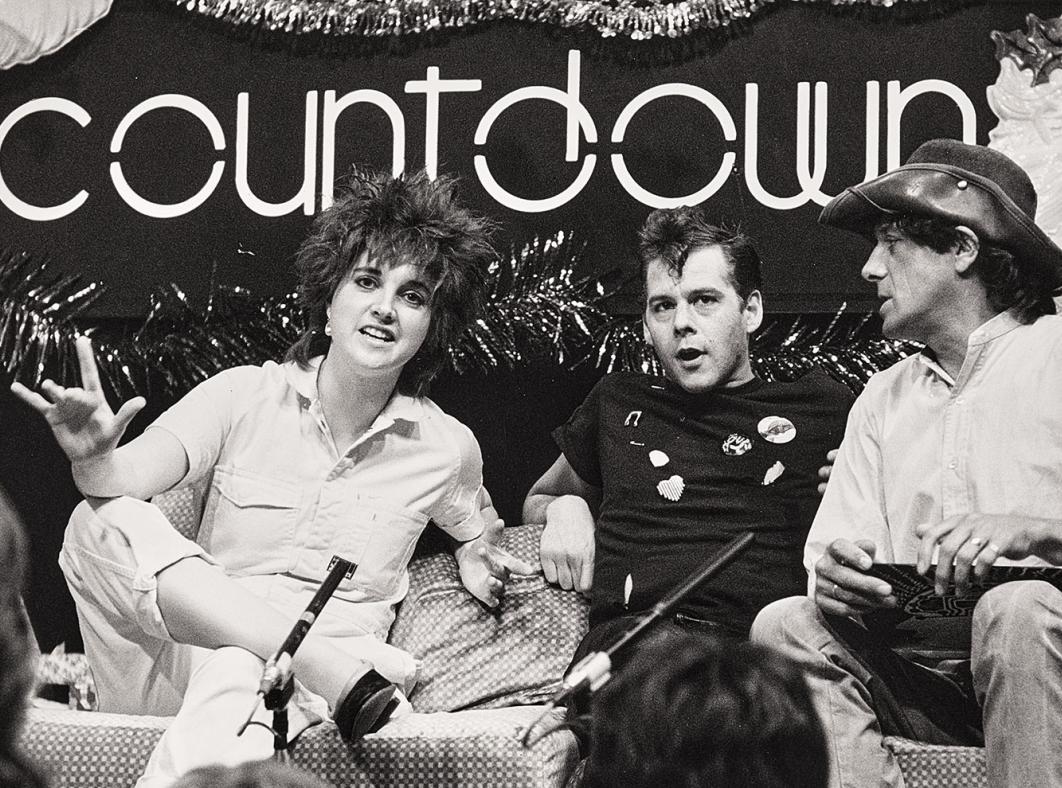 Three people sitting on a couch in a tv studio under a sign that says 'countdown'
