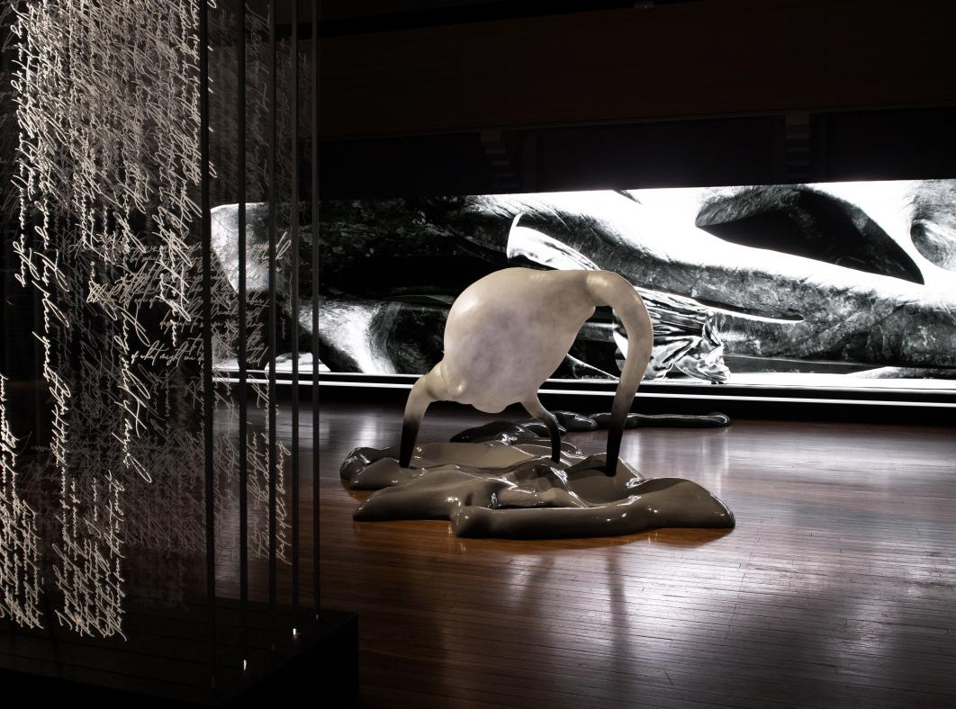 Detail from the art installation Inferno at the NFSA featuring a vertical screen with dense handwriting, a white sculpture arising from a mass on the floor, and a long screen showing a black-and-white landscape.