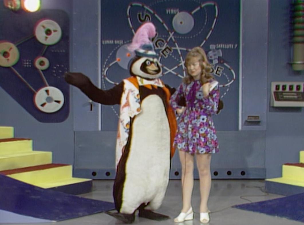 Two brightly dressed presenters stand in a studio