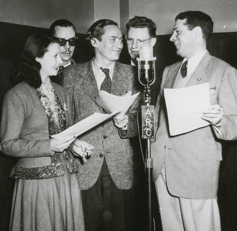 Vivien Leigh, Peter Finch and Laurence Olivier holding scripts and gathered around a radio microphone