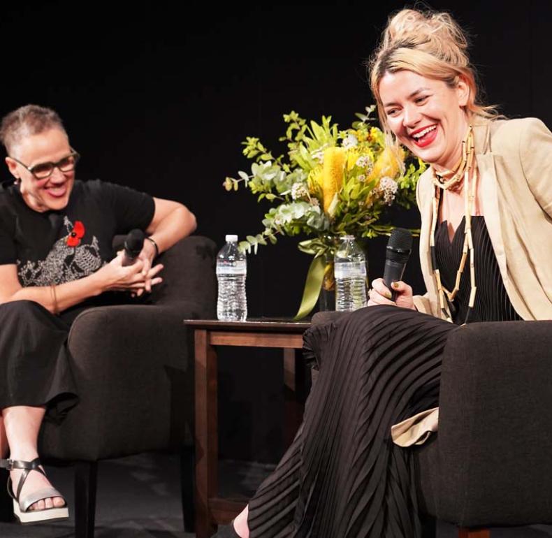 Artist Jazz Money in conversation at the NFSA, seated next to a table with a vase of flowers on it. Both Jazz and the interviewer are laughing
