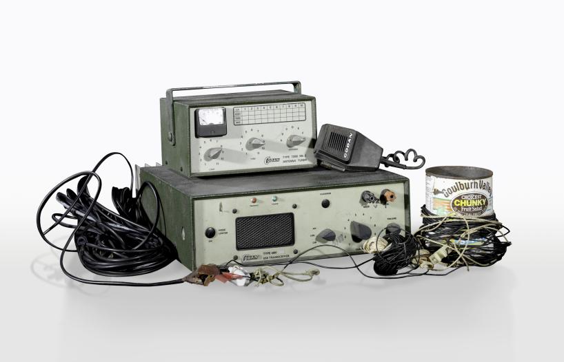 A collection of homemade radio equipment including a transceiver box with knobs and speaker, an antenna tuner, cords and a fruit salad tin used as an antenna.