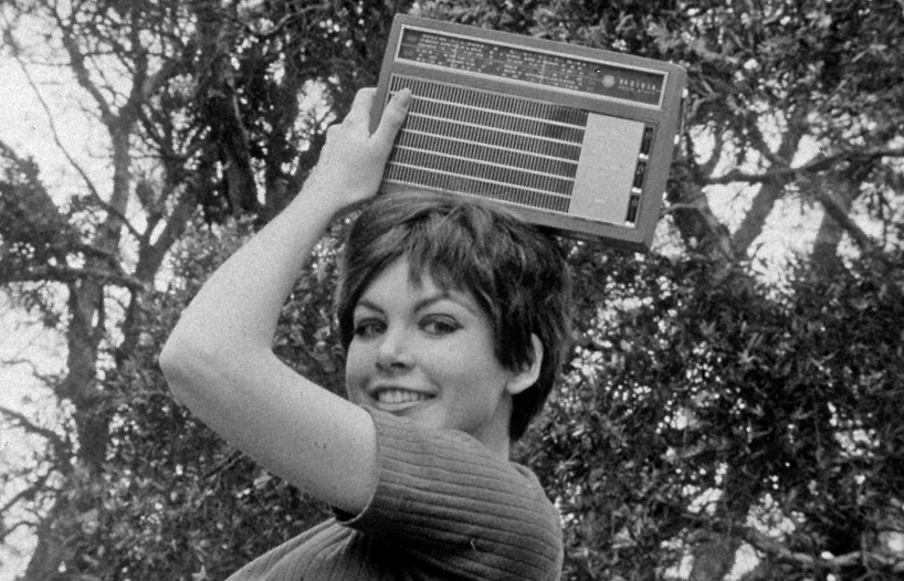 A young woman holding a transistor radio on top of her head and posing for the camera
