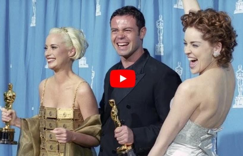 Costume designers Lizzy Gardiner and Tim Chappel holding Academy Awards backstage at the Oscars ceremony with Sharon Stone. They are all smiling and laughing and Gardiner is wearing a dress made out of gold American Express credit cards.