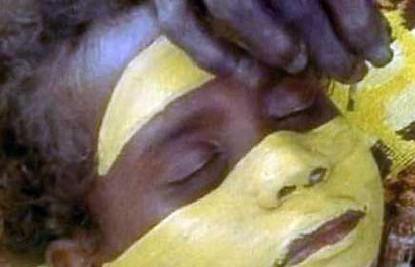 A young Indigenous boy lying down getting his face painted for a ceremony.
