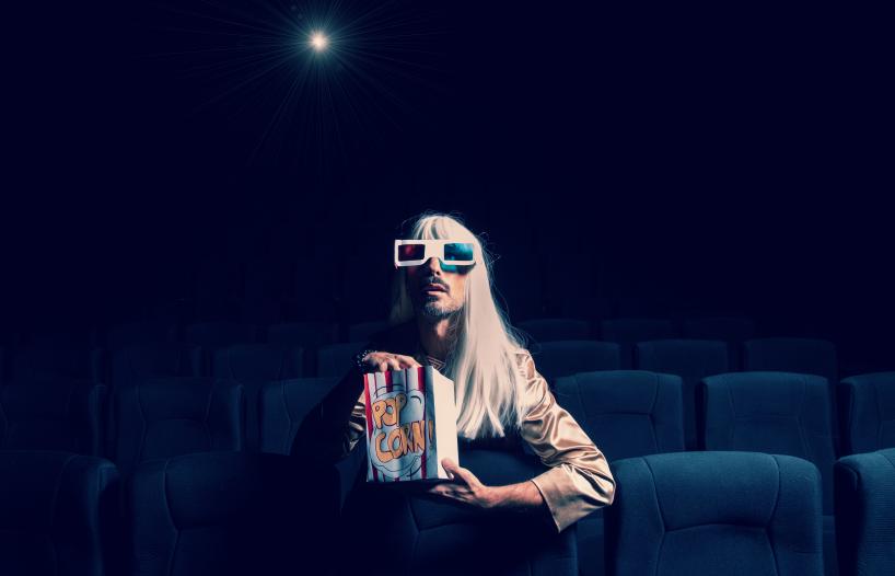 Person sitting in empty cinema wearing 3D glasses and eating popcorn