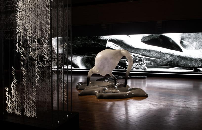 Detail from the art installation Inferno at the NFSA featuring a vertical screen with dense handwriting, a white sculpture arising from a mass on the floor, and a long screen showing a black-and-white landscape.