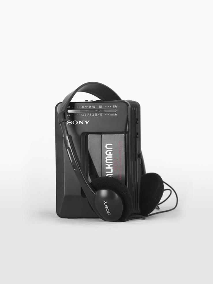 A black Sony Walkman portable radio and cassette player with headphones sitting on top of it.