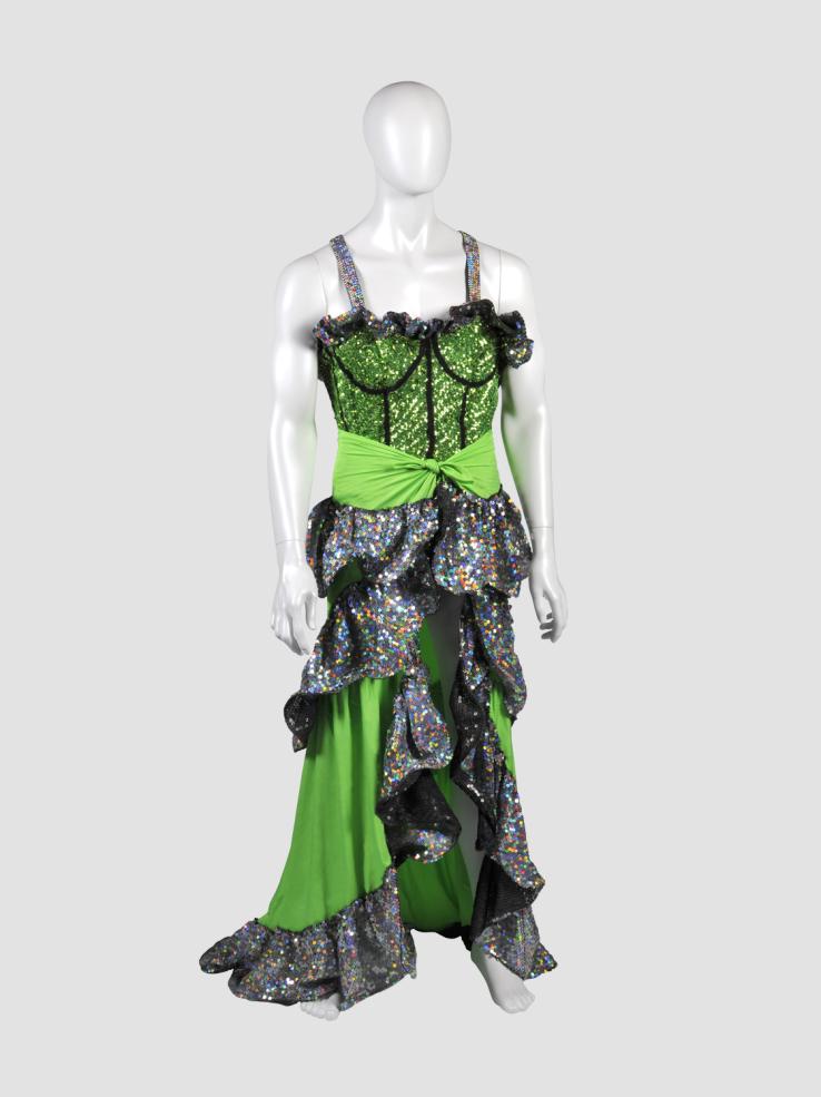 A white manequin wearing a sequinned green costume with frilly detailing on the bodice and skirt