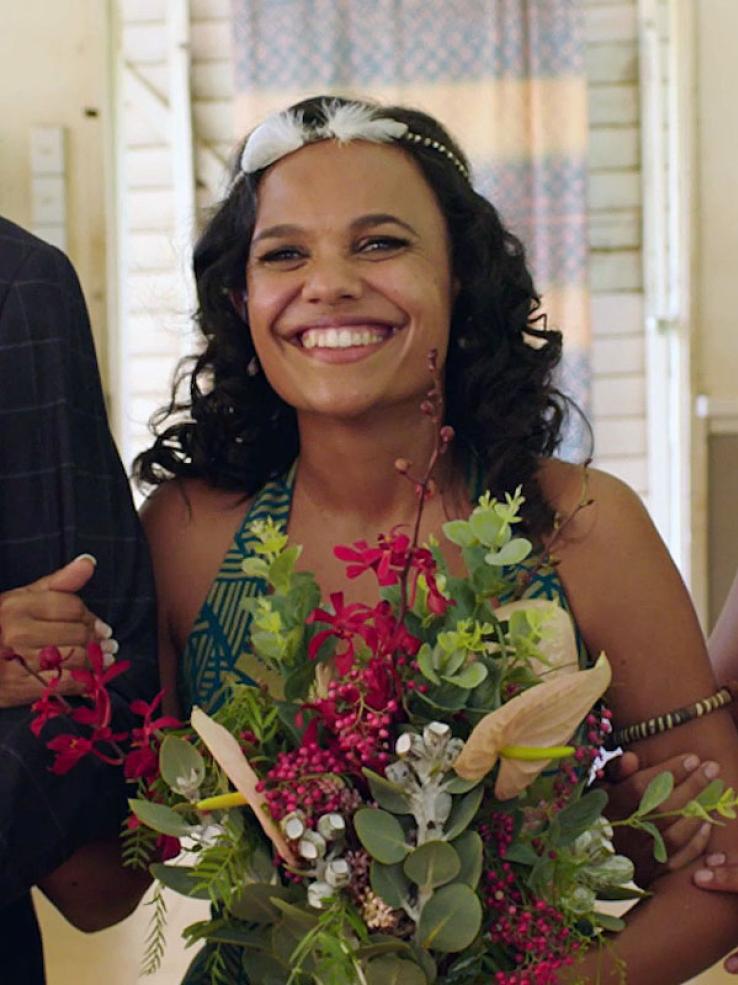 Close up of actor Miranda Tapsell holding a wedding bouquet and smiling.
