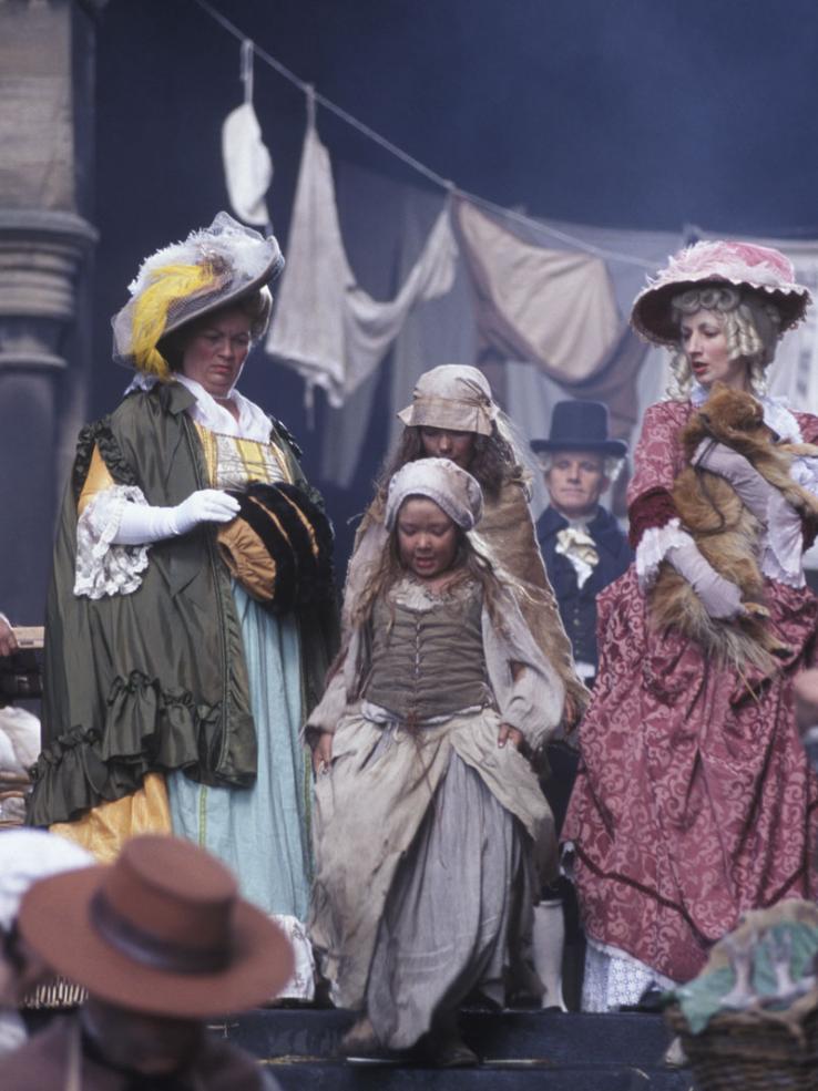 Two women in fancy 18th century dresses and bonnets look on in distaste as two girls in dirty street clothes pass between them.