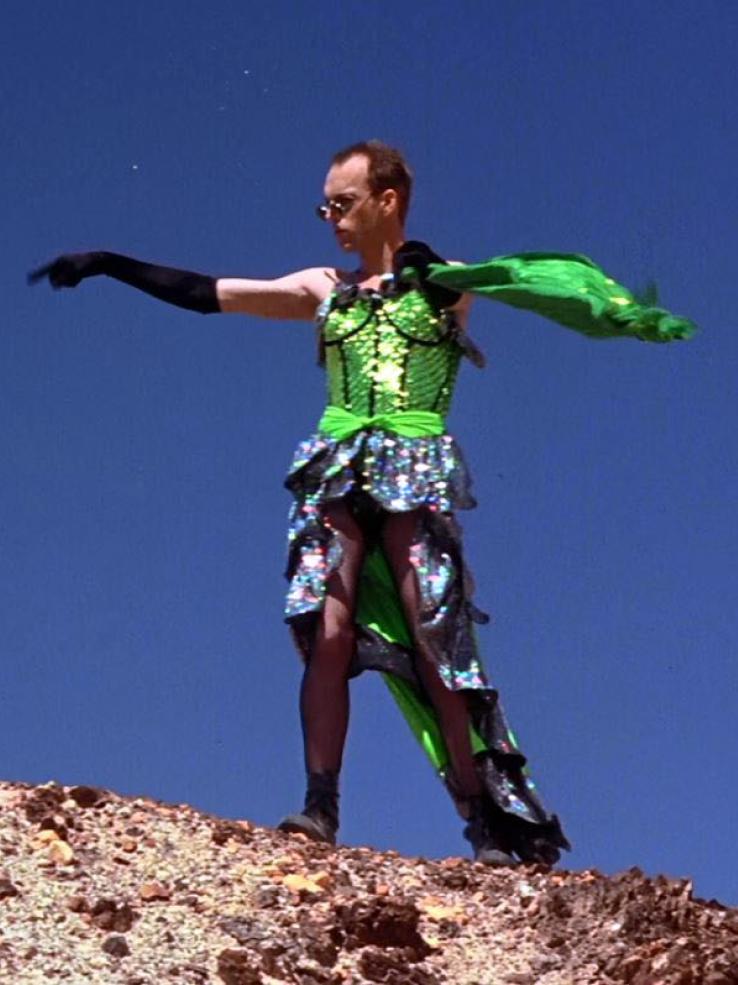 Hugo Weaving in dressed in green sequined dress dancing on a mountain in the desert