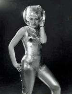 Woman in a gold jumpsuit with a fish bowl on her head as a helmet