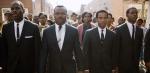 A group of African American people, led by four men wearing suits and ties, marching in the street.