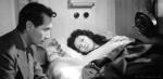 A woman lying in bed and a man sits next to her