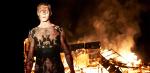A young man covered in ash and blood standing in front of a house on fire at night time