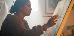 A young woman sitting at an easel painting onto a canvas.