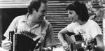 A man playing an according seated next to a woman playing guitar.