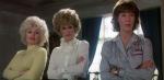 Three women (actors Dolly Parton, Jane Fonda and Lily Tomlin) standing side by side each with their arms folded looking at something off camera.