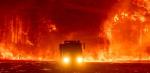Silhouette of a fire truck surrounded by bushland that is on fire and glowing orange.