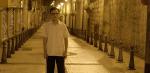 A man standing alone on an empty street at night time.