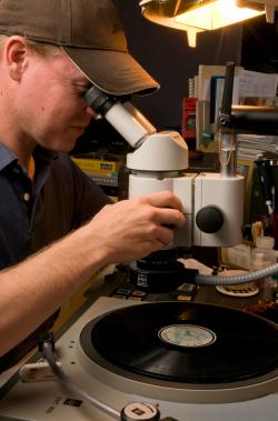 Technician using a binocular microscope for repairing a vinyl disc.
