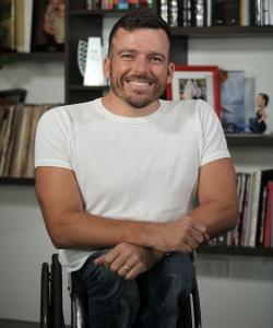 Kurt Fearnley Paralympics hero A portrait of wheelchair racer Kurt Fearnley smiling for the camera. He has bookshelves filled with books behind him.