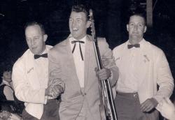 Col Joye holding his guitar being led away by two men in white jackets and black bow ties. Col Joye holding his guitar being led away by two men in white jackets and black bow ties.