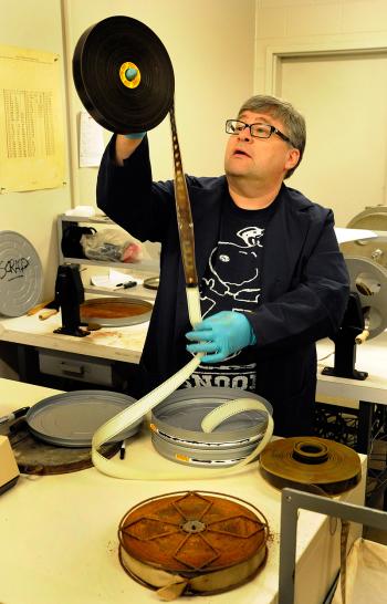 Nitrate Vault Leader, George Willeman, inspecting a reel of nitrate film. A badly decomposed reel can be seen on the table in the foreground.