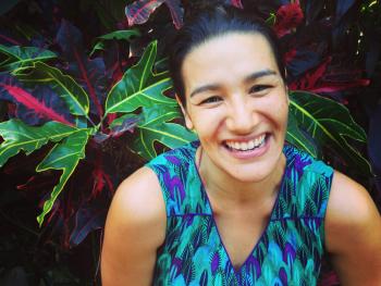 Author Clare Atkins smiling. She is standing in front of a plant with large leaves.