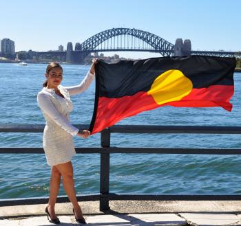 Cheree Toka holding an Australian Aboriginal flag. The Sydney Harbour Bridge is in the background.