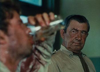 A policeman watches a grubby man covered in sweat and grime downing a glass of beer