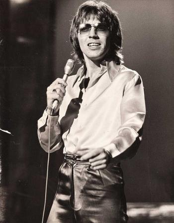 Three-quarter image of singer Stevie Wright holding a microphone and standing on a stage.