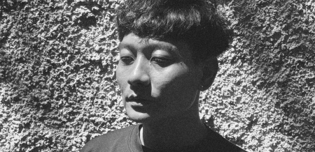 A black-and-white image of a man standing in front of a wall with his eyes closed